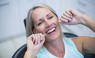 Woman flossing teeth in Massapequa Park