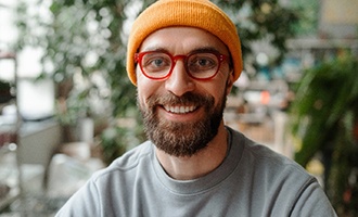 a smiling man wearing orange glasses and an orange beanie