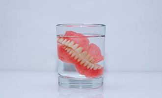 Dentures soak in glass of clear liquid
