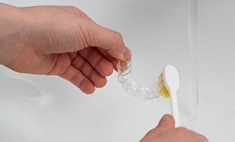 Patient cleaning clear aligner in sink