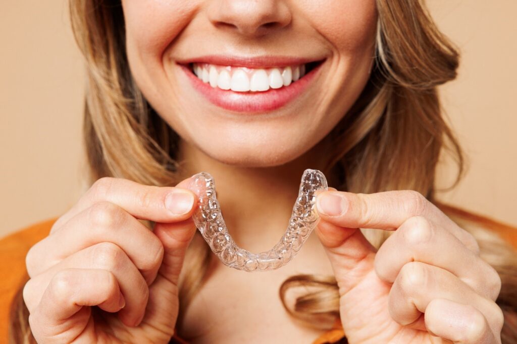 Woman smiling while holding clear aligner