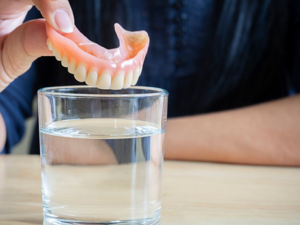 Close up of person dropping dentures into cleaning solution