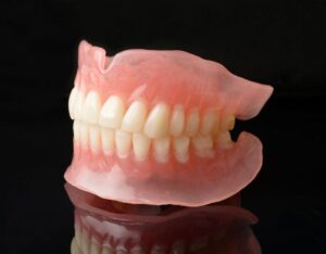 Full set of dentures closed together on a reflective surface with black background